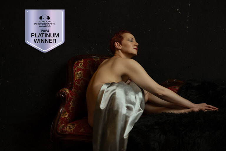 A person draped in a white cloth sits on a vintage chair against a dark background. A "2024 Platinum Winner" badge from the London Photography Awards is displayed. Tanya Eivin Photography