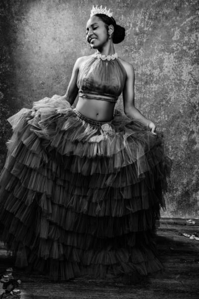 A woman wearing a tiara and a layered tulle skirt poses against a textured backdrop in a black and white photo. Tanya Eivin Photography