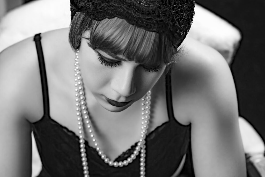 Black and white photo of a senior in high school in vintage attire with a lace headband, pearl necklace, and dark dress, looking down with eyes closed. senior portraits Austin Texas