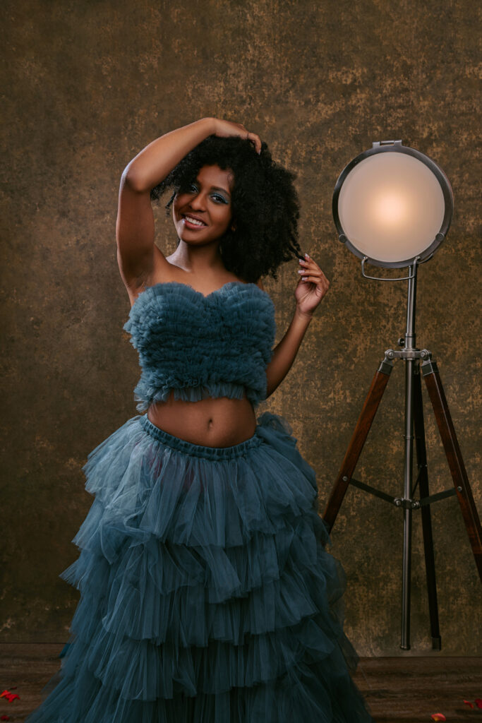 a girl in a blue dress standing by a studio light for her senior pictures