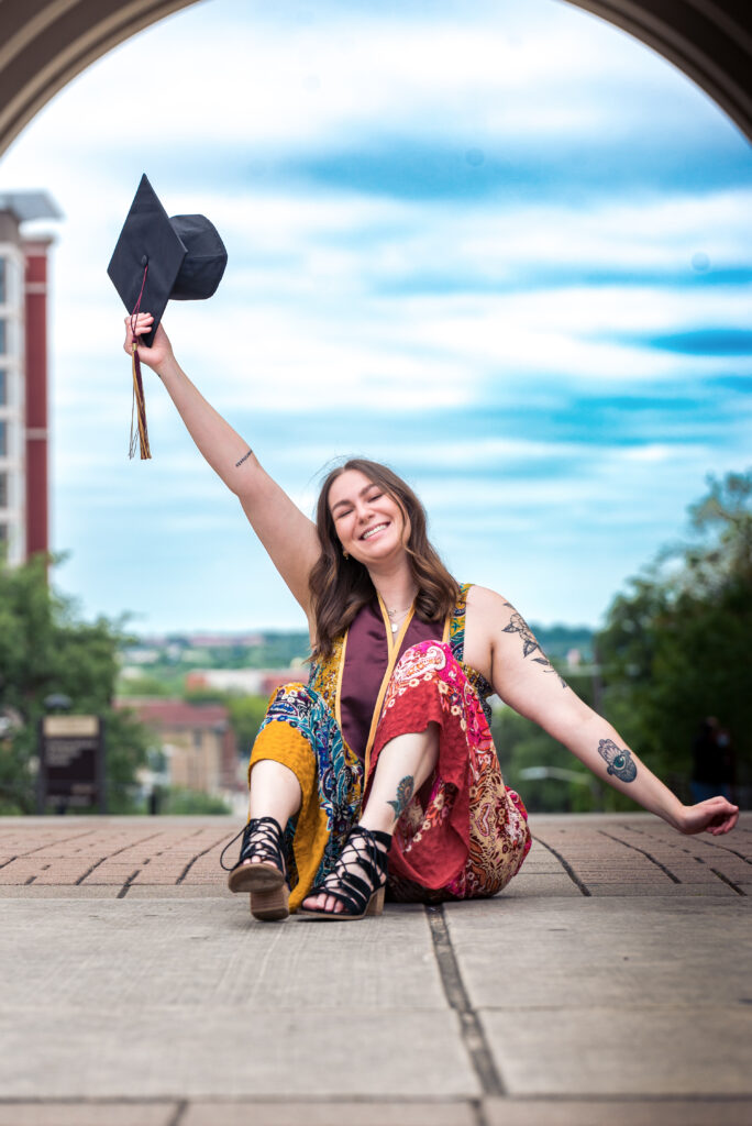 a girl sitting in an archway with a cap in the air for her austin texas senior photos